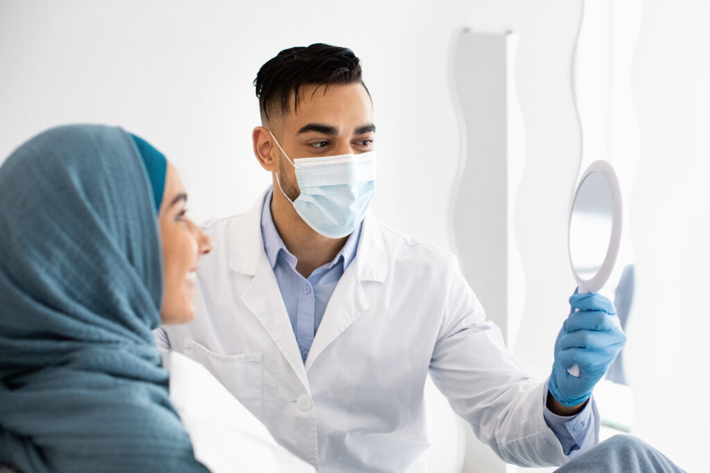 Arab Stomatologist Holding Mirror, Showing Teeth Treatment Result To Muslim Lady Patient During Check Up In Modern Clinic, Islamic Woman In Hijab Enjoying Her Beautiful Smile, Closeup Shot