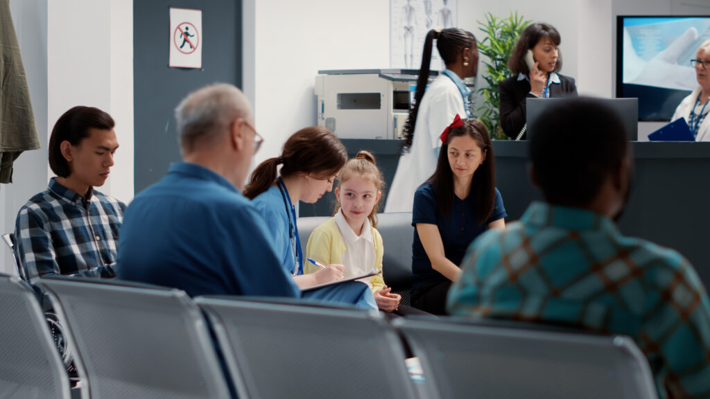 Health specialist talking to small child and mother in hospital reception lobby, taking notes about consultation. Nurse consulting little girl sitting in facility waiting room, healthcare support.