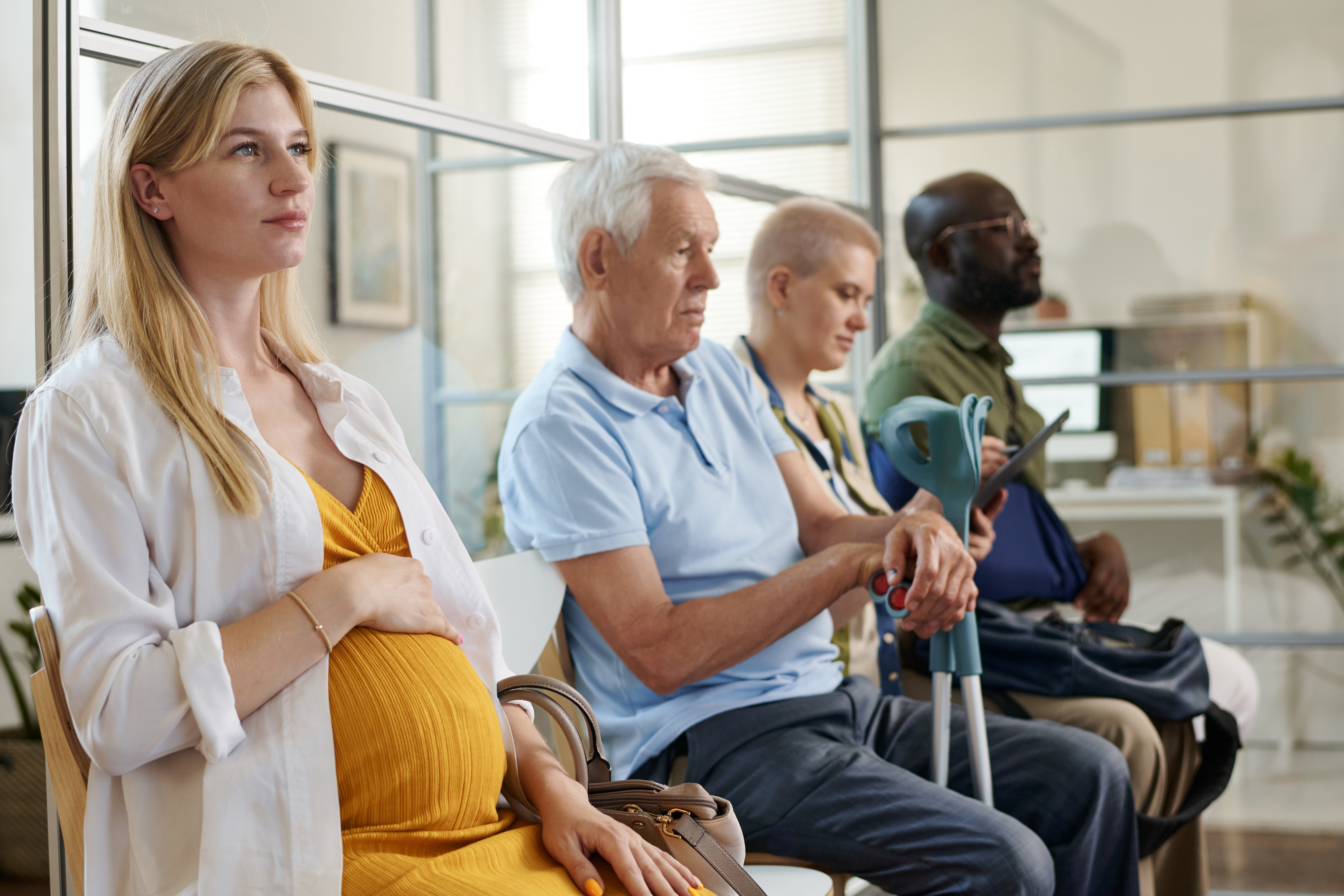 Young pregnant woman sitting in a queue with other people and waiting for consultation in office